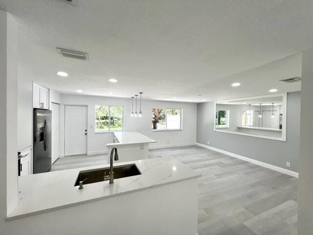 kitchen with light stone countertops, stainless steel fridge, sink, light hardwood / wood-style flooring, and white cabinets