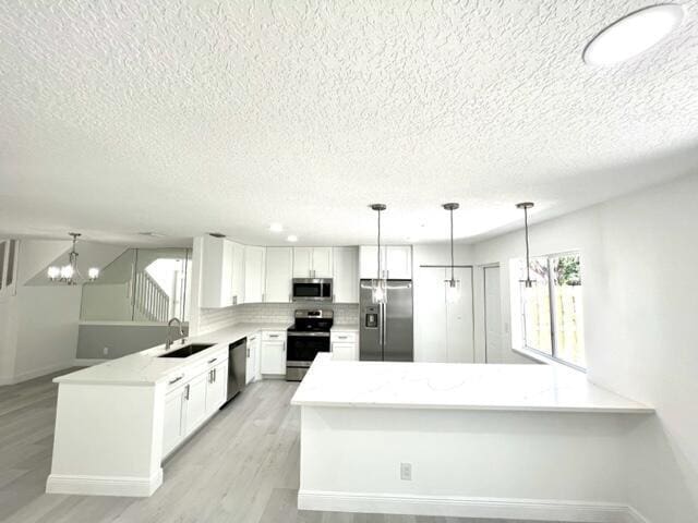 kitchen featuring white cabinetry, hanging light fixtures, light stone counters, and appliances with stainless steel finishes