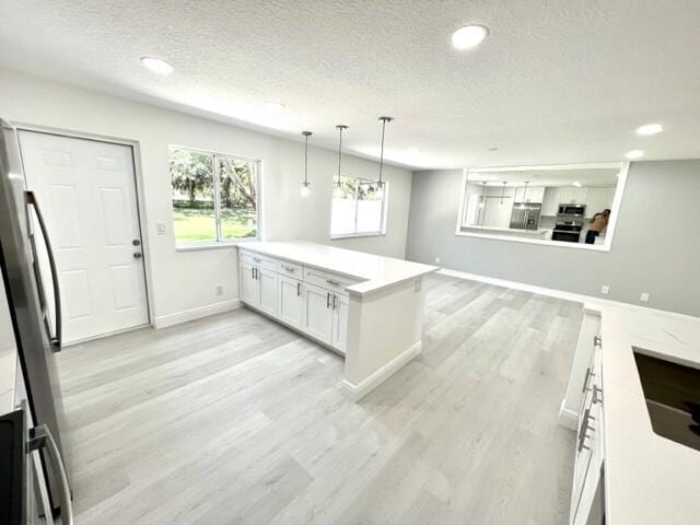 kitchen with a textured ceiling, stainless steel appliances, pendant lighting, light hardwood / wood-style flooring, and white cabinetry