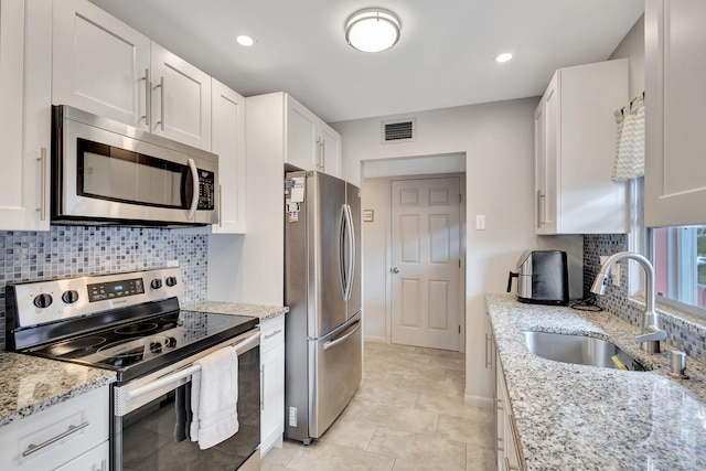 kitchen with decorative backsplash, appliances with stainless steel finishes, light stone counters, sink, and white cabinets