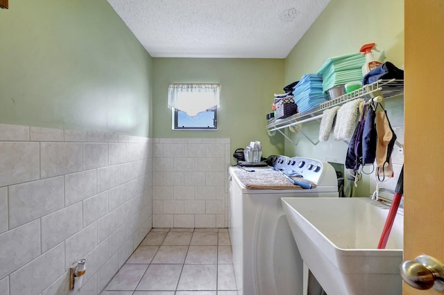 washroom with sink, light tile patterned floors, tile walls, washing machine and dryer, and a textured ceiling