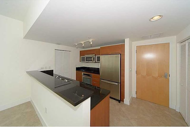 kitchen with sink, stainless steel appliances, kitchen peninsula, track lighting, and light tile patterned flooring