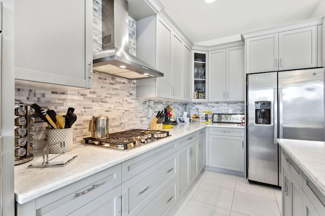 kitchen featuring backsplash, light tile patterned flooring, light stone countertops, stainless steel appliances, and wall chimney exhaust hood