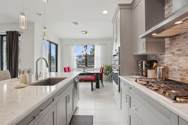 kitchen featuring appliances with stainless steel finishes, backsplash, decorative light fixtures, wall chimney range hood, and sink