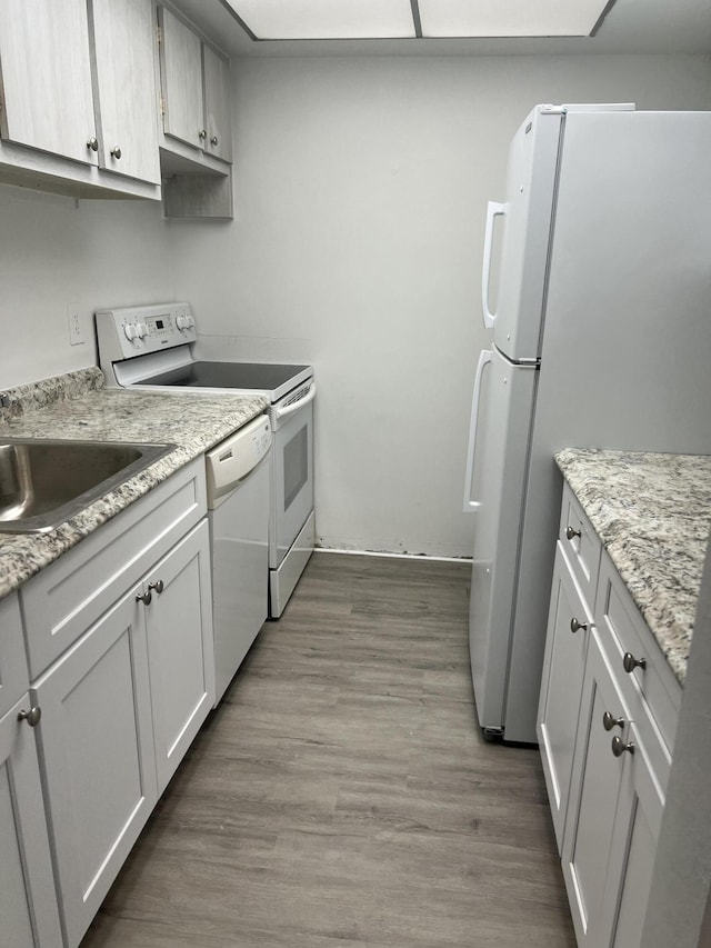 kitchen featuring light stone countertops, white appliances, sink, light hardwood / wood-style floors, and white cabinetry