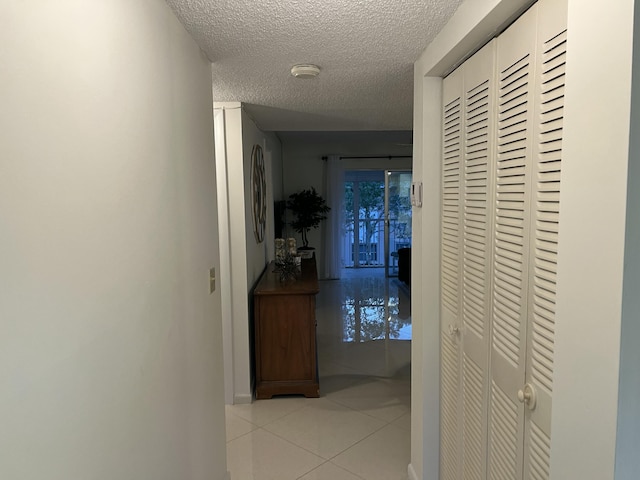 hall featuring tile patterned floors, baseboards, and a textured ceiling