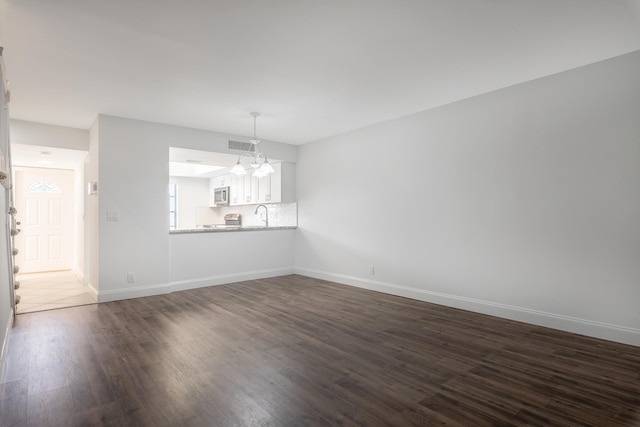 unfurnished living room with dark hardwood / wood-style flooring, a chandelier, and sink