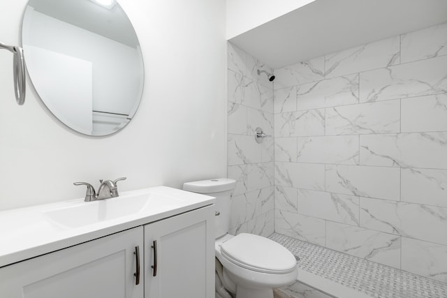 bathroom featuring a tile shower, vanity, and toilet