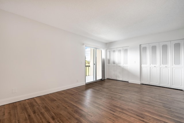 unfurnished bedroom featuring a textured ceiling, access to exterior, dark wood-type flooring, and multiple closets