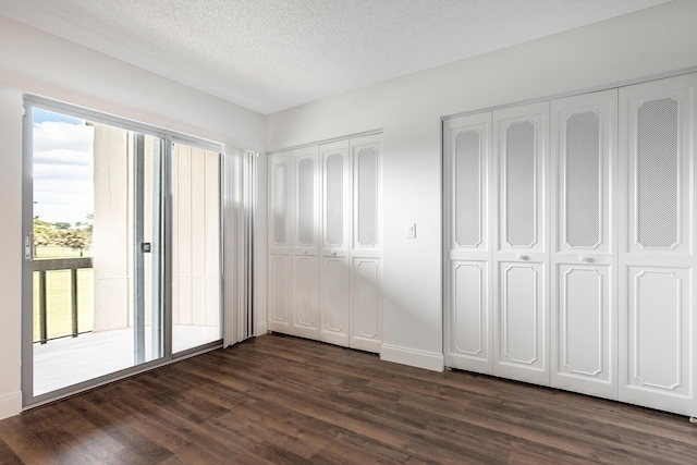 unfurnished bedroom with access to exterior, a textured ceiling, multiple closets, and dark wood-type flooring