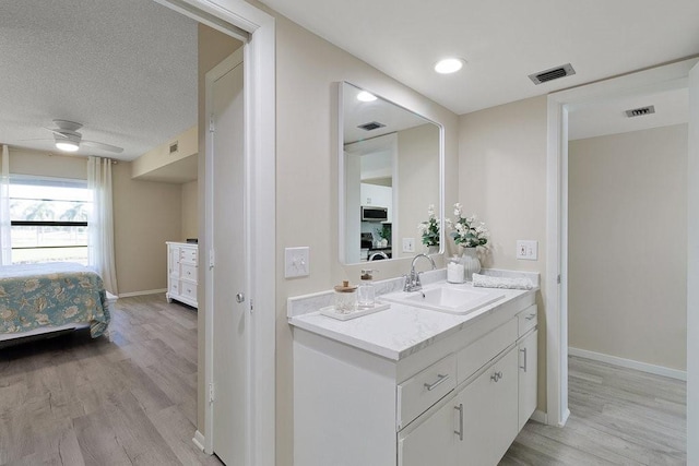 bathroom featuring vanity, ceiling fan, wood-type flooring, and a textured ceiling