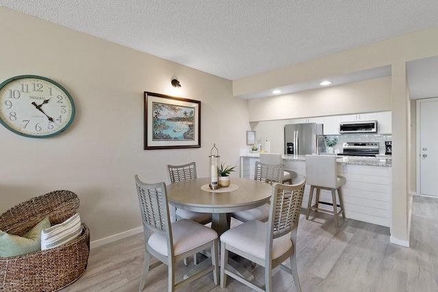 dining room with light wood-type flooring and a textured ceiling