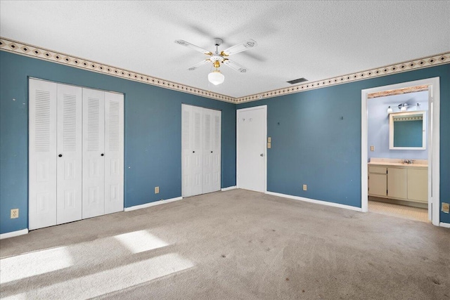 unfurnished bedroom featuring two closets, visible vents, a sink, a textured ceiling, and baseboards