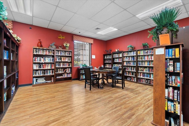 office space with wall of books, wood finished floors, and a paneled ceiling