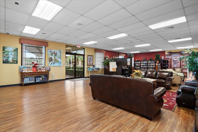 living area featuring a paneled ceiling, wood finished floors, visible vents, and baseboards