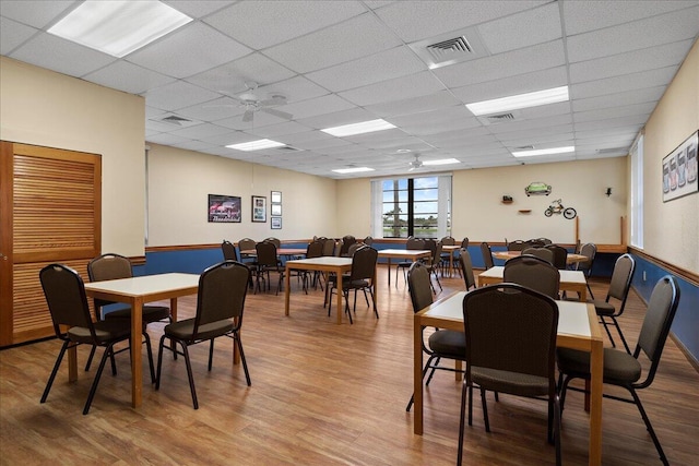 dining space with a ceiling fan, light wood-type flooring, visible vents, and a drop ceiling