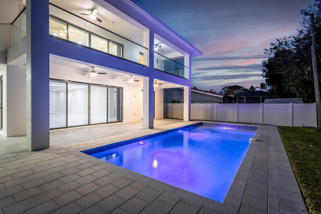 pool at dusk featuring ceiling fan and a patio