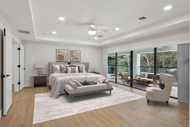 bedroom featuring light wood-type flooring, ceiling fan, access to exterior, and a tray ceiling