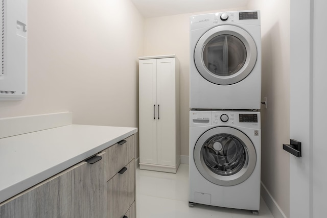 laundry area featuring cabinets, light tile patterned flooring, and stacked washer and clothes dryer