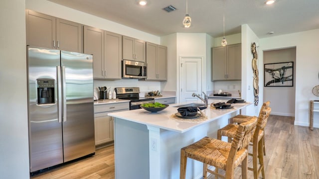 kitchen with gray cabinetry, sink, stainless steel appliances, decorative light fixtures, and light wood-type flooring