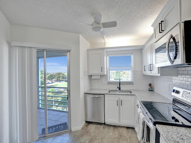 kitchen with appliances with stainless steel finishes, light wood-type flooring, sink, white cabinetry, and tasteful backsplash