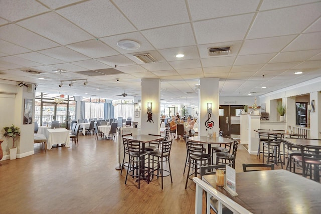 dining area featuring ceiling fan, a drop ceiling, and wood-type flooring