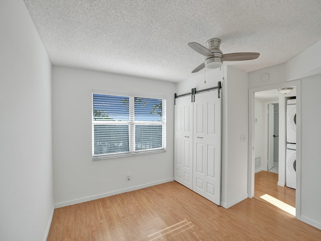 unfurnished bedroom with stacked washing maching and dryer, a closet, light wood-type flooring, a barn door, and ceiling fan