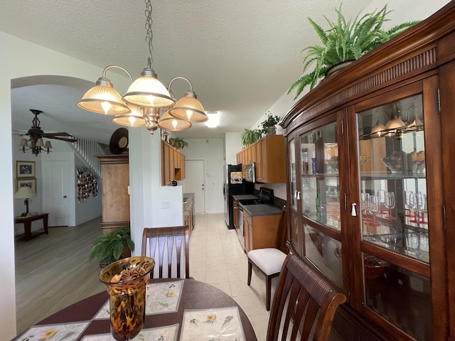 dining space with light tile patterned floors, arched walkways, a textured ceiling, and ceiling fan with notable chandelier