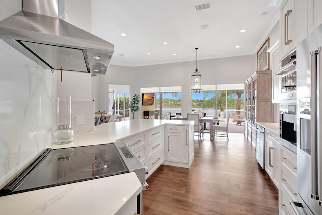 kitchen with kitchen peninsula, dark hardwood / wood-style flooring, hanging light fixtures, range hood, and white cabinets