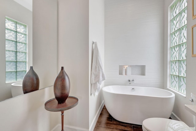 bathroom featuring toilet, plenty of natural light, a washtub, and hardwood / wood-style flooring