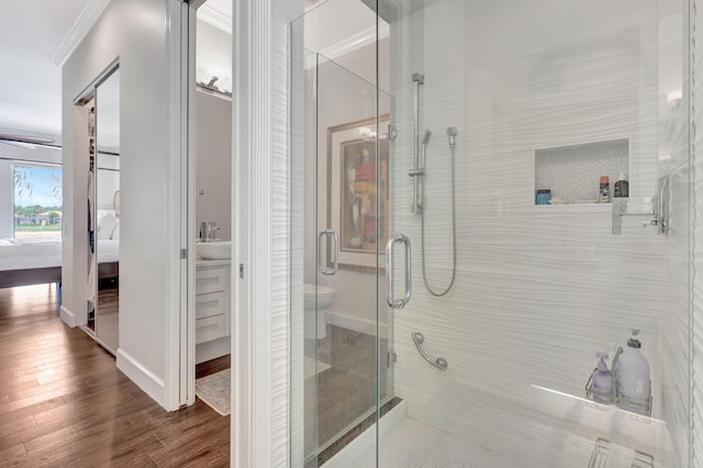 bathroom featuring toilet, a shower with door, wood-type flooring, crown molding, and sink