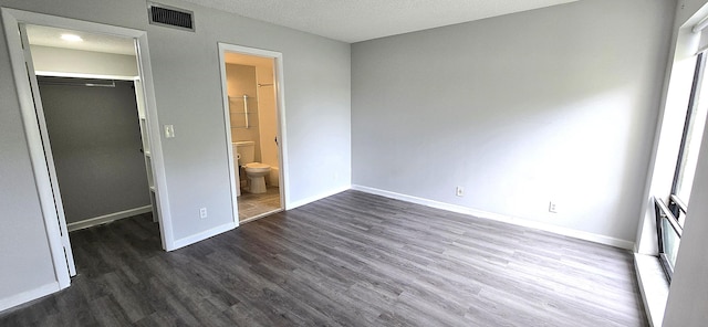 unfurnished bedroom featuring a walk in closet, dark hardwood / wood-style flooring, connected bathroom, and a closet