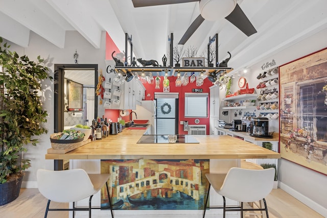 kitchen with butcher block counters, stainless steel fridge, a breakfast bar, light wood-type flooring, and beamed ceiling