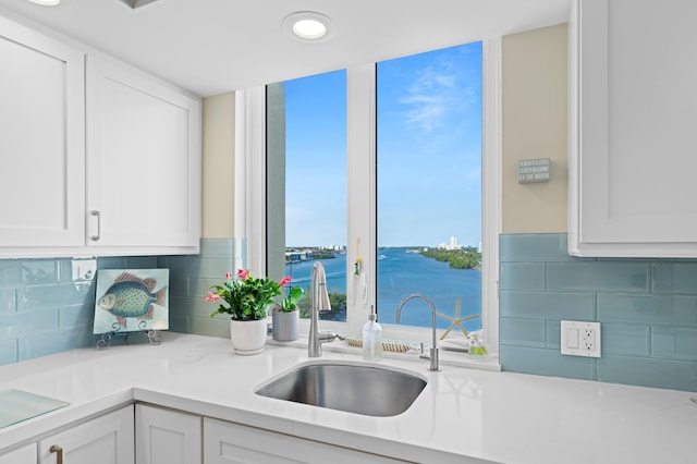 kitchen featuring sink, backsplash, white cabinetry, and a water view