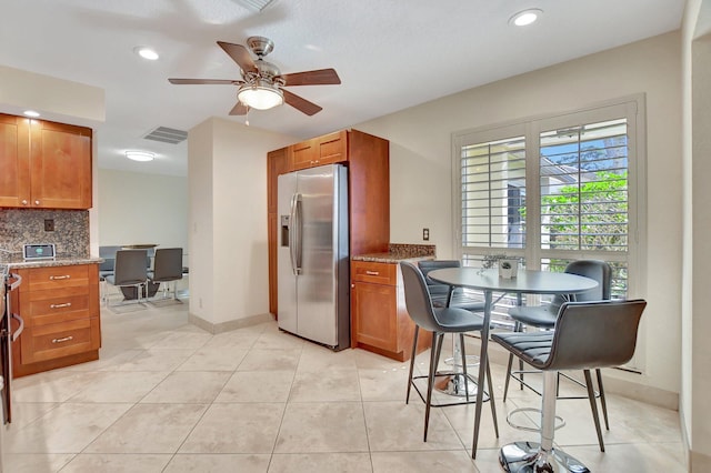 kitchen with stainless steel fridge, backsplash, light stone counters, ceiling fan, and light tile patterned flooring