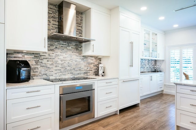 2897 SE Saint Lucie Blvd, Stuart, FL 34997 - kitchen featuring decorative backsplash, stainless steel oven, black electric stovetop, wall chimney range hood, and light wood-type flooring