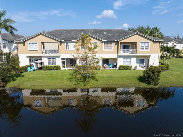 rear view of house with a water view, a balcony, and a lawn