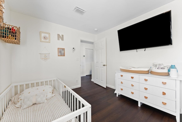 bedroom with a nursery area and dark wood-type flooring