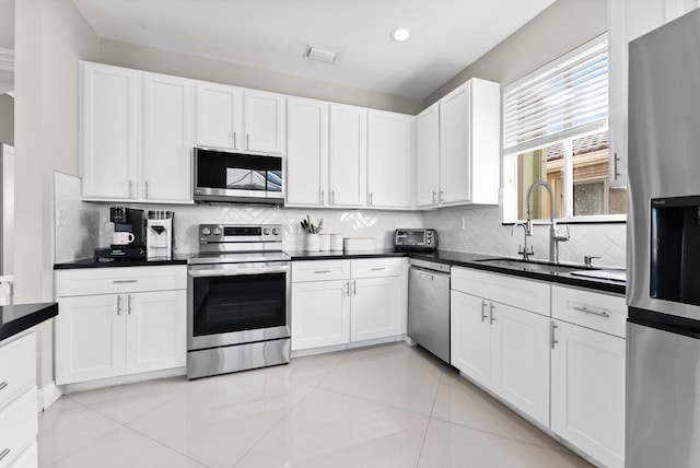 kitchen with stainless steel appliances, white cabinetry, light tile patterned floors, and sink