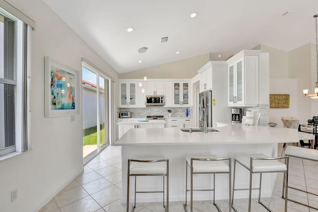 kitchen with stainless steel appliances, a breakfast bar, white cabinetry, decorative light fixtures, and lofted ceiling