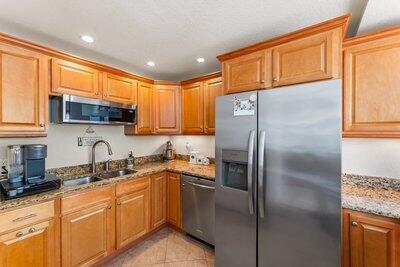 kitchen with appliances with stainless steel finishes, sink, light tile patterned floors, and light stone counters