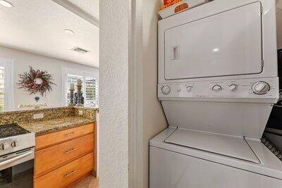 clothes washing area featuring laundry area, stacked washer and dryer, visible vents, and a wealth of natural light