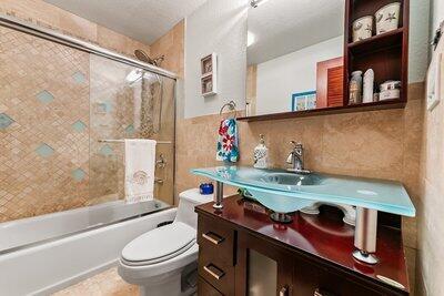 full bathroom with tile walls, vanity, enclosed tub / shower combo, and toilet