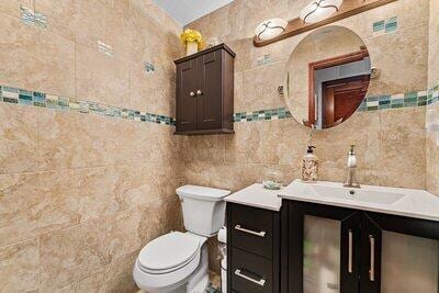 half bath featuring toilet, tile walls, and vanity