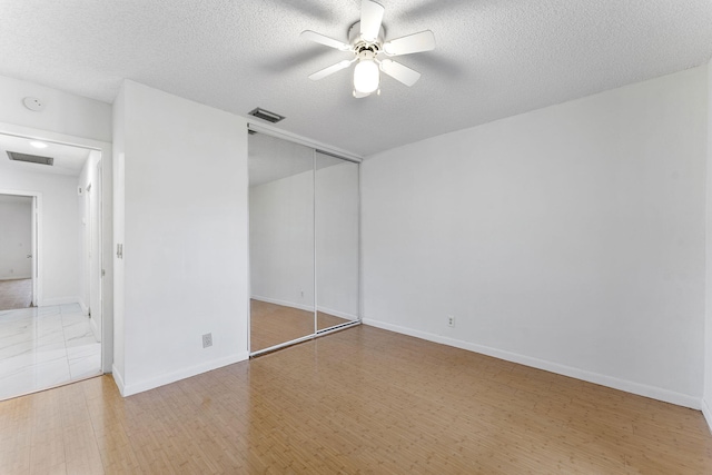 unfurnished bedroom with wood-type flooring, ceiling fan, a textured ceiling, and a closet