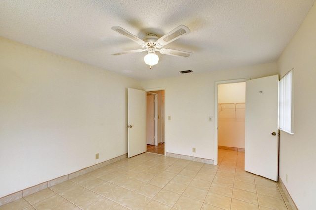 unfurnished bedroom with ceiling fan, a walk in closet, light tile patterned floors, and a closet