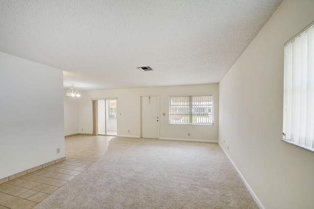 empty room featuring light colored carpet, a textured ceiling, and an inviting chandelier