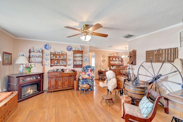 living area with ceiling fan with notable chandelier, a textured ceiling, light hardwood / wood-style floors, and crown molding