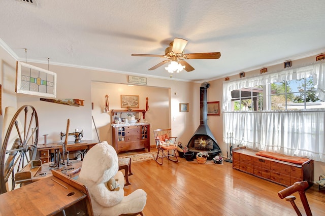 living area with crown molding, ceiling fan, a wood stove, hardwood / wood-style flooring, and a textured ceiling