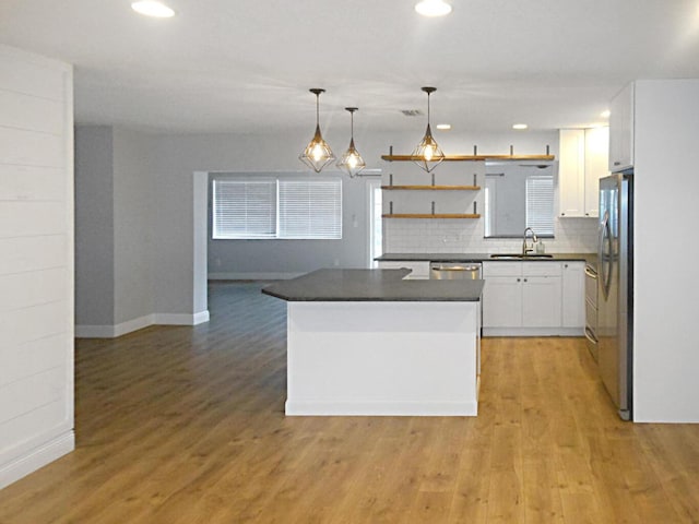 kitchen with sink, white cabinetry, hanging light fixtures, appliances with stainless steel finishes, and light hardwood / wood-style floors